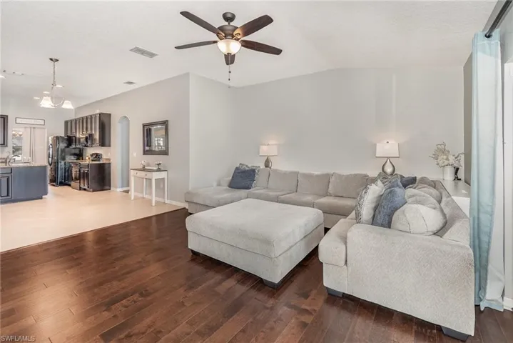 Living area featuring vaulted ceiling, arched walkways, visible vents, a ceiling fan, and wood finished floors