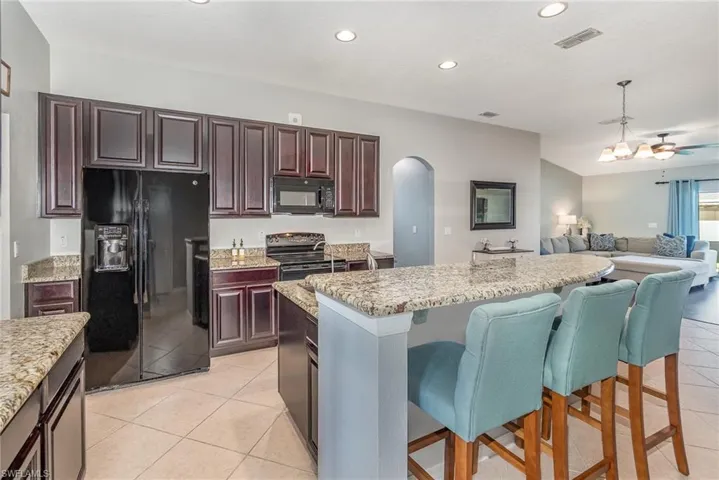 Kitchen with visible vents, arched walkways, open floor plan, black appliances, and a kitchen breakfast bar