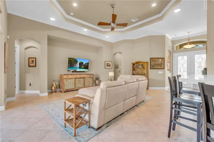 Tiled living room with a raised ceiling, crown molding, french doors, and ceiling fan