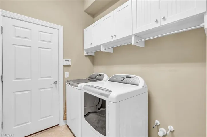 Clothes washing area featuring washer and dryer, cabinets, and light tile patterned floors