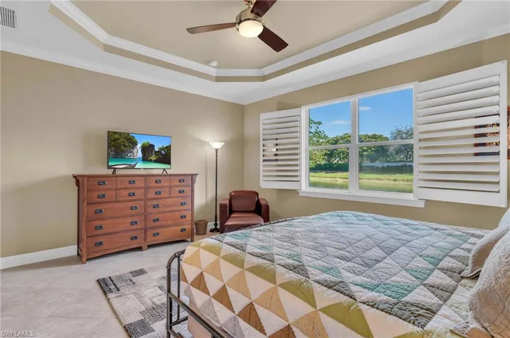 Bedroom with light tile patterned floors, a tray ceiling, ceiling fan, and ornamental molding