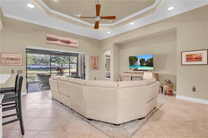 Living room with ceiling fan, ornamental molding, light tile patterned floors, and a tray ceiling