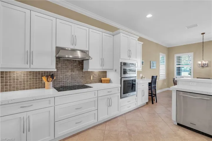 Kitchen with stainless steel appliances, crown molding, light tile patterned floors, white cabinets, and hanging light fixtures