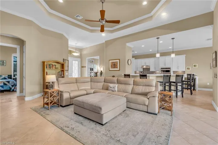 Living room with light tile patterned floors, a raised ceiling, ceiling fan, and ornamental molding
