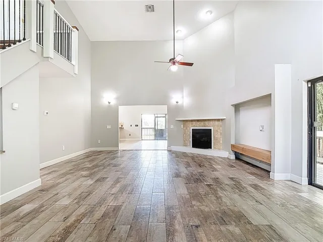 Unfurnished living room with a tiled fireplace, a towering ceiling, light wood finished floors, ceiling fan, and a baseboard radiator