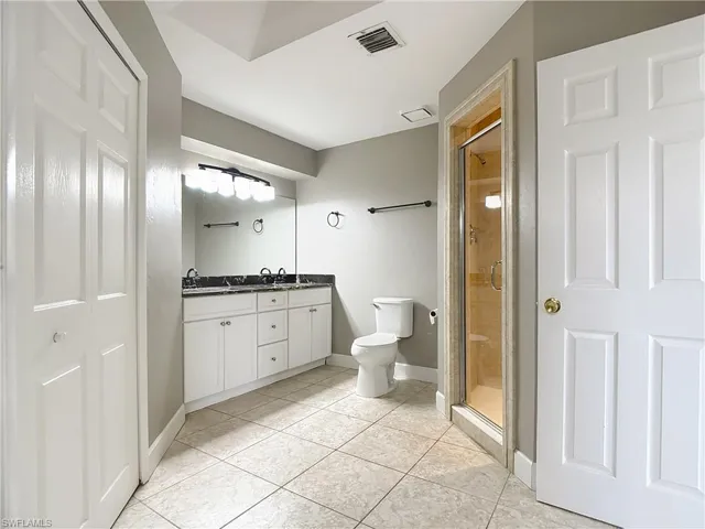 Full bath featuring double vanity, a shower stall, light tile patterned floors, and a closet