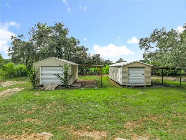 View of grassy yard with a shed, view of wooded area, and a carport
