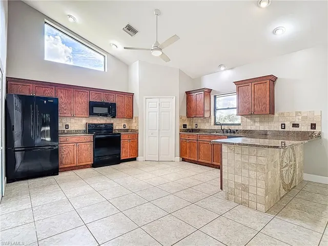 Kitchen with backsplash, black appliances, a peninsula, high vaulted ceiling, and light tile patterned floors