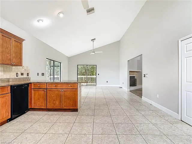 Kitchen featuring brown cabinets, a fireplace, decorative backsplash, a ceiling fan, and high vaulted ceiling