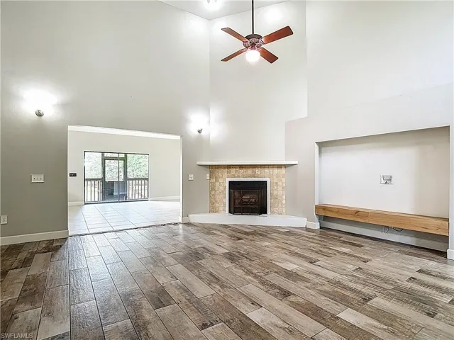 Unfurnished living room with a high ceiling, wood finished floors, ceiling fan, and a fireplace