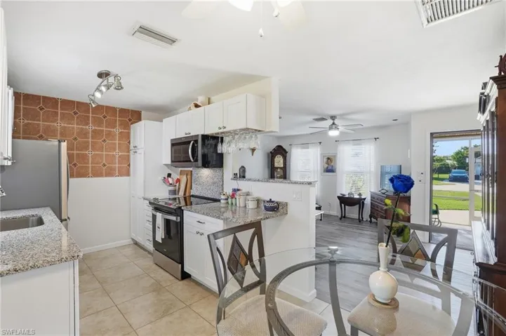 Kitchen with light stone countertops, white cabinetry, stainless steel appliances, wallpapered walls, and light tile patterned floors