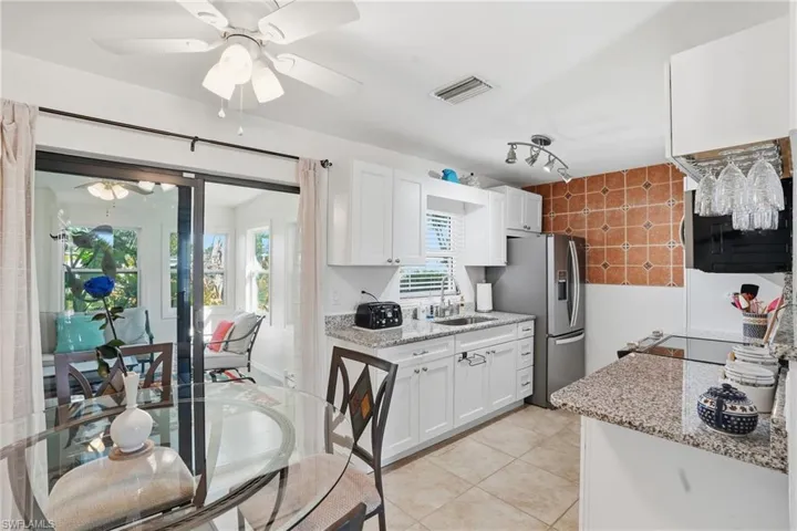 Kitchen with light stone counters, white cabinets, stainless steel refrigerator with ice dispenser, light tile patterned floors, and a ceiling fan