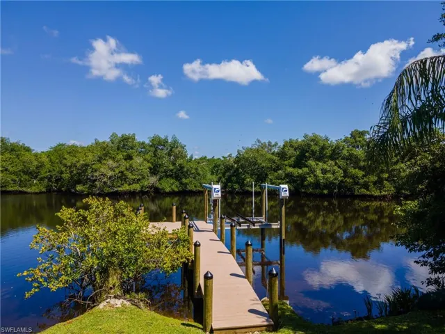 Waterfront property featuring a composite dock with boat lift, integrated pilings, and lush green landscaping