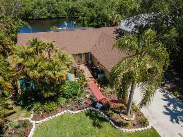Waterfront property featuring a private dock, lush tropical landscaping, mature palm trees, a well-maintained lawn, and a paved driveway