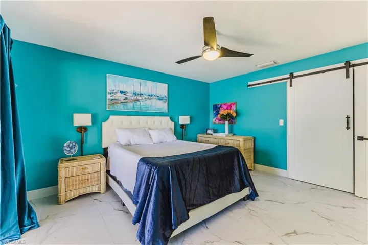 Spacious room featuring a white barn door, marble-look flooring, ceiling fan with integrated lighting, and vibrant wall color