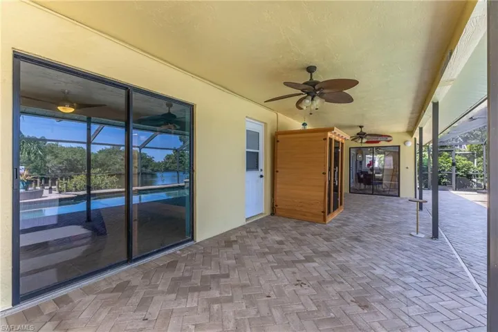 Expansive covered patio featuring herringbone-patterned paver flooring, multiple ceiling fans, and large sliding glass doors opening to a screened pool area with water views