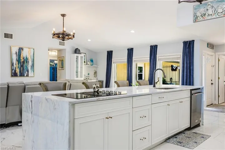Expansive kitchen island featuring a waterfall countertop, integrated cooktop, undermount sink with a gooseneck faucet, and white cabinetry