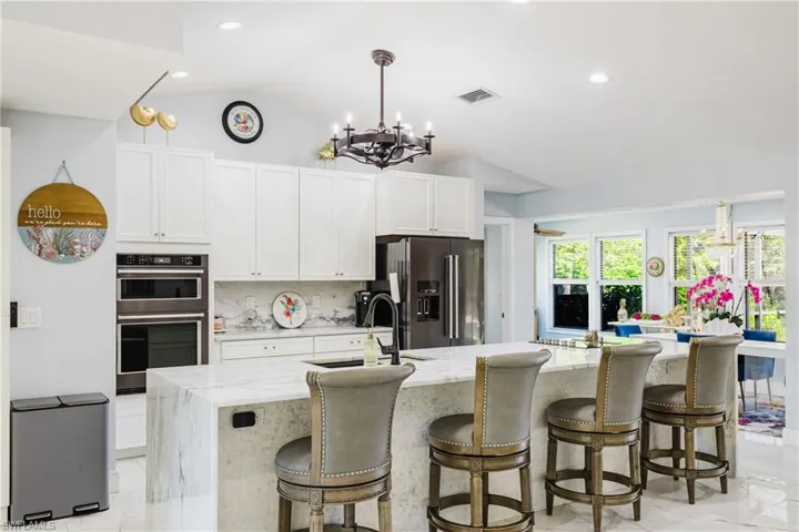 Gourmet kitchen with a large waterfall island featuring a marble-finish countertop, white cabinetry, integrated double ovens, and a dark stainless steel refrigerator