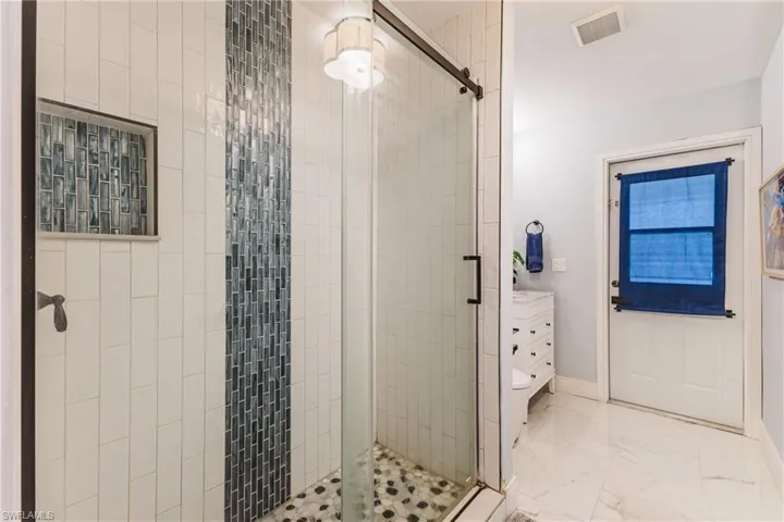 Walk-in shower featuring subway tile, a mosaic accent strip, and a built-in niche