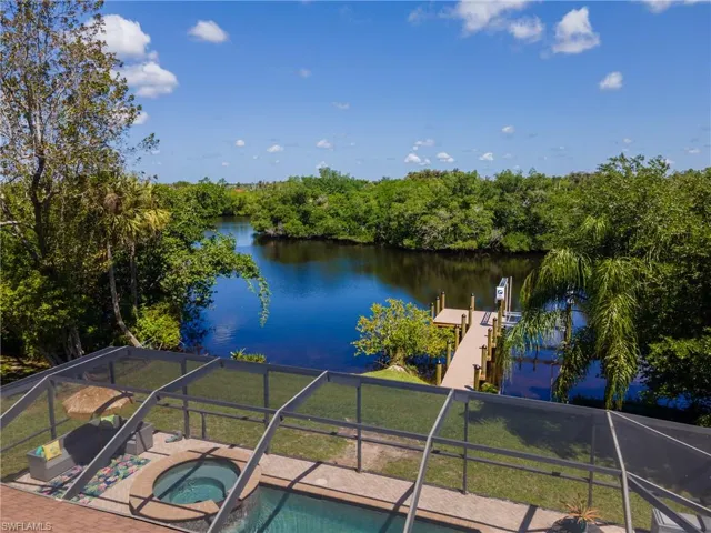 Waterfront property featuring a private dock with a boat lift, a screened lanai encompassing a pool and spa, and a natural perimeter of lush vegetation