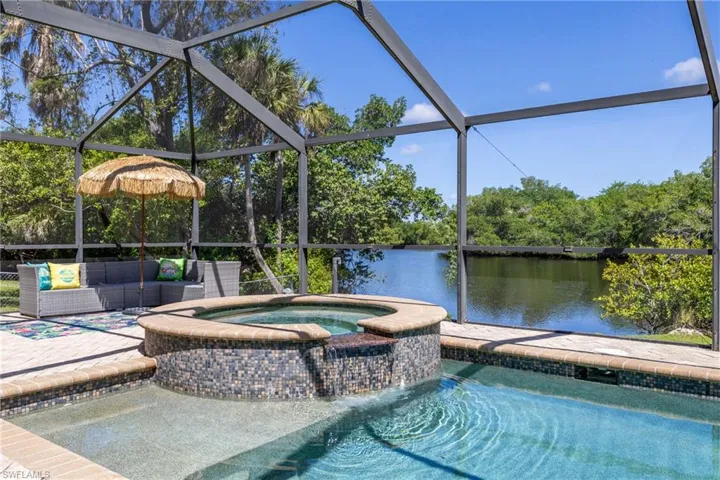 Screened enclosure featuring a mosaic-tiled hot tub with a water feature, a swimming pool, and a paver deck