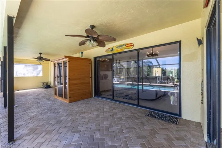 Expansive covered patio featuring herringbone paver flooring, multiple ceiling fans, and a built-in sauna with a glass door