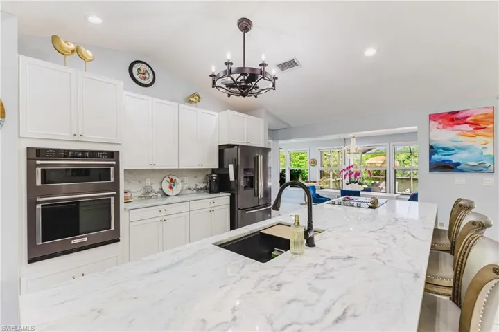 Expansive kitchen island with a light-toned, veined countertop, featuring an undermount sink and matte black faucet