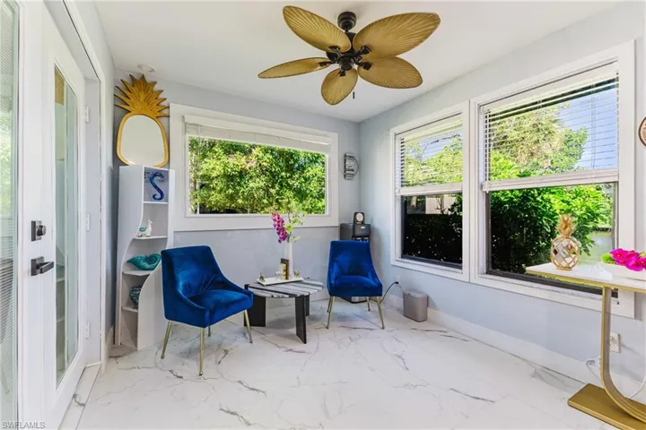 Light-filled sunroom featuring white tile flooring, multiple windows, a ceiling fan with palm-leaf inspired blades, and a glass-paneled door
