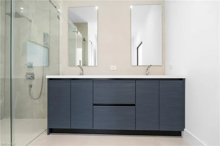 Bathroom featuring a marble finish shower, double vanity, and light tile patterned flooring