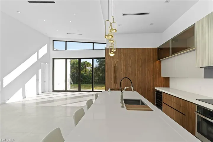 Kitchen featuring brown cabinetry, modern cabinets, stainless steel oven, pendant lighting, and light stone counters