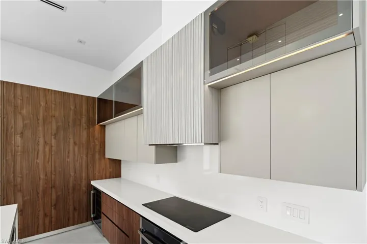 Kitchen featuring modern cabinets, black electric stovetop, wooden walls, stainless steel oven, and wine cooler