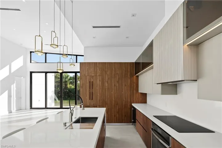 Kitchen with modern cabinets, brown cabinetry, hanging light fixtures, oven, and light stone countertops
