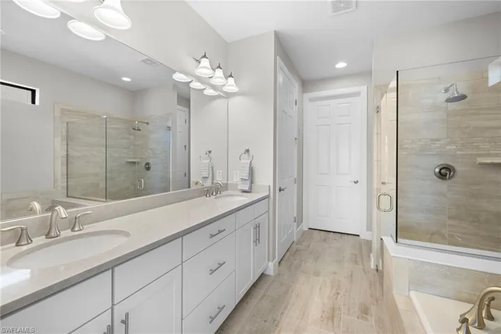 Primary bathroom featuring a stall shower, double vanity, and light wood-style floors