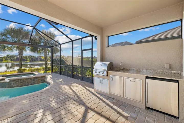 View of patio / terrace featuring an outdoor kitchen, glass enclosure, a sunroom, a water view, and a pool with connected hot tub