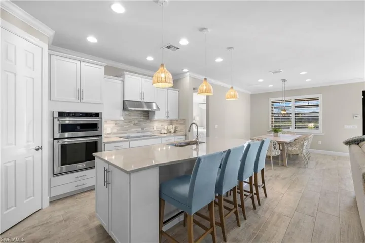 Kitchen featuring decorative light fixtures, tasteful backsplash, crown molding, a kitchen breakfast bar, and white cabinets