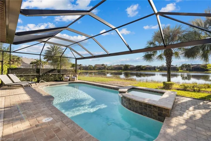 View of swimming pool with glass enclosure, a sunroom, a pool with connected hot tub, a water view, and a patio