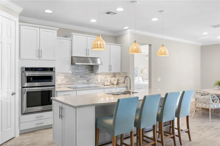 Kitchen with crown molding, backsplash, double oven, a kitchen breakfast bar, and white cabinetry