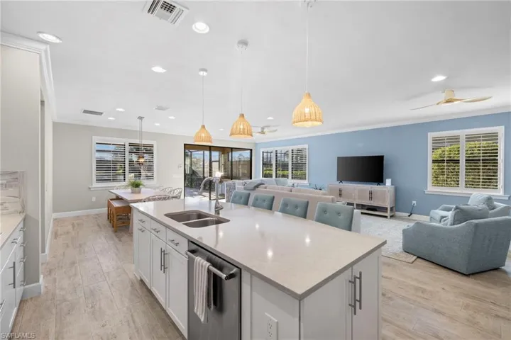 Kitchen with ornamental molding, white cabinetry, open floor plan, pendant lighting, and light stone counters
