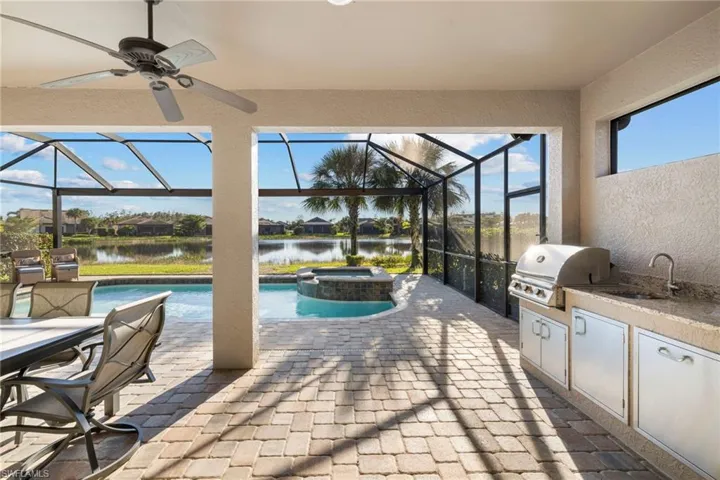View of patio with a outdoor kitchen, enclosure, exterior kitchen, a pool with connected hot tub, and a water view