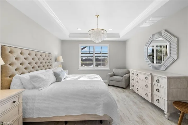 Primary Bedroom on ground floor featuring light wood-style floors, multiple windows, a raised ceiling, a chandelier, and recessed lighting