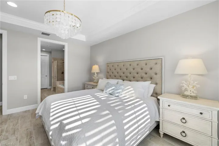 Bedroom featuring ensuite bath, a tray ceiling, light wood-type flooring, a chandelier, and crown molding