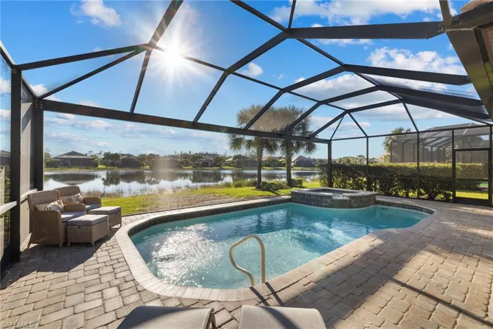 View of swimming pool featuring a sunroom, a lanai, a water view, a pool with connected hot tub, and a patio area