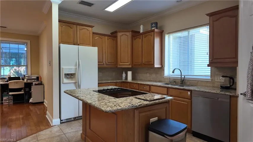 Kitchen with ornamental molding, light stone countertops, white fridge with ice dispenser, dishwasher, and brown cabinetry