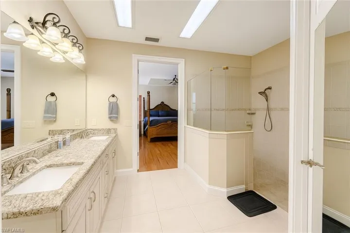 Ensuite bathroom featuring a walk in shower, double vanity, light tile patterned floors, and a ceiling fan