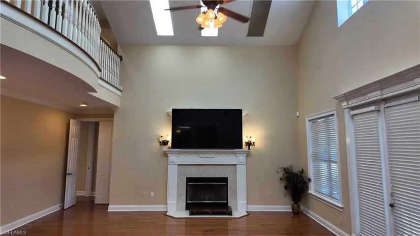 Unfurnished living room with a high ceiling, a tile fireplace, dark wood-style floors, a ceiling fan, and a skylight
