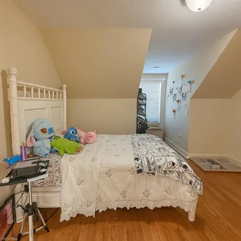 Bedroom with wood finished floors, vaulted ceiling, and a textured ceiling