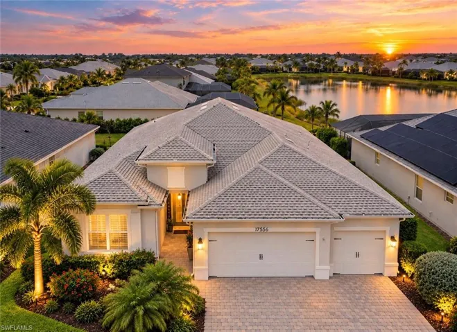 Stucco exterior with a multi-gable roof, paver driveway, three-car garage, and established landscaping