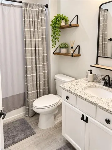 White vanity with black hardware, stone-finish countertop, undermount sink, and black faucet