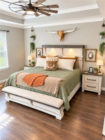 Tray ceiling with crown molding, wood-finish flooring, and a ceiling fan with light fixture