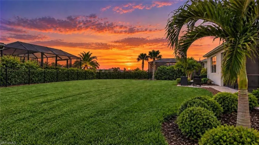 Expansive lawn with mature palm trees, perimeter fencing, and a screened enclosure